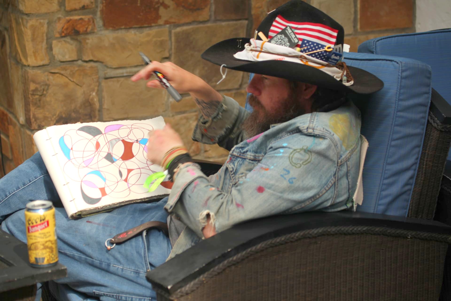 Artist in a cowboy hat drawing colorful overlapping circles in a sketchbook